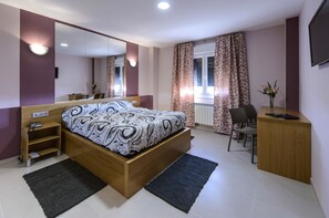 Un dormitorio con cama, escritorio, silla, espejo y ventana con cortinas.