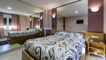 Una habitación de hotel moderna con una cama grande, otra cama más pequeña, un espejo, un televisor y una mesita de noche.