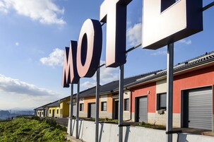 Un motel con un gran letrero que dice 'MOTEL', edificios modernos y un cielo despejado.