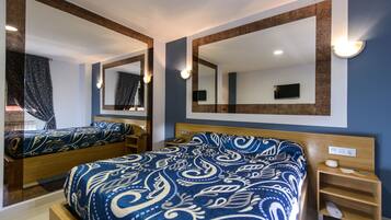 A hotel room with two beds, a large mirror, and a television on the wall.