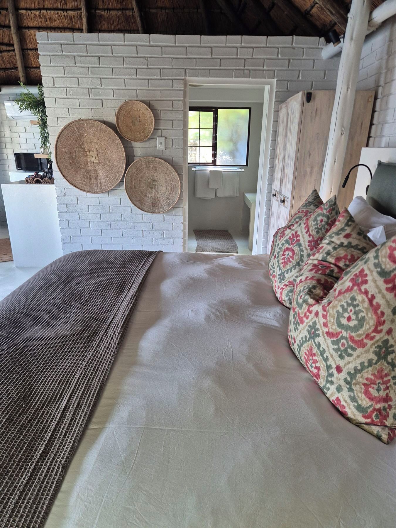 A bedroom with a bed, a woven rug, a patterned pillow, and a brick wall.