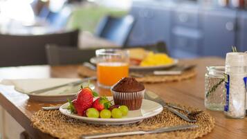 A breakfast table with a plate of strawberries, grapes, and a muffin, a glass of orange juice, and a jar of sugar.