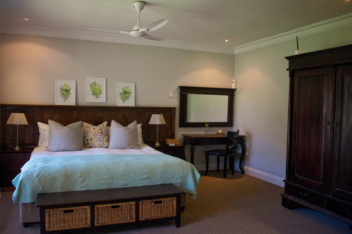 A bedroom with a bed, bedside tables, a desk, a chair, a wardrobe, and a ceiling fan.