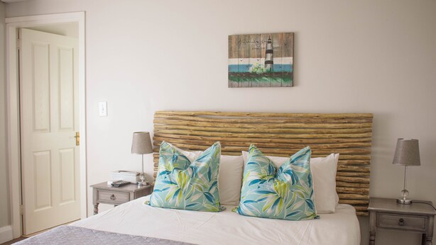Een slaapkamer met een groot bed, twee nachtkastjes, een houten hoofdbord en een schilderij van een vuurtoren.