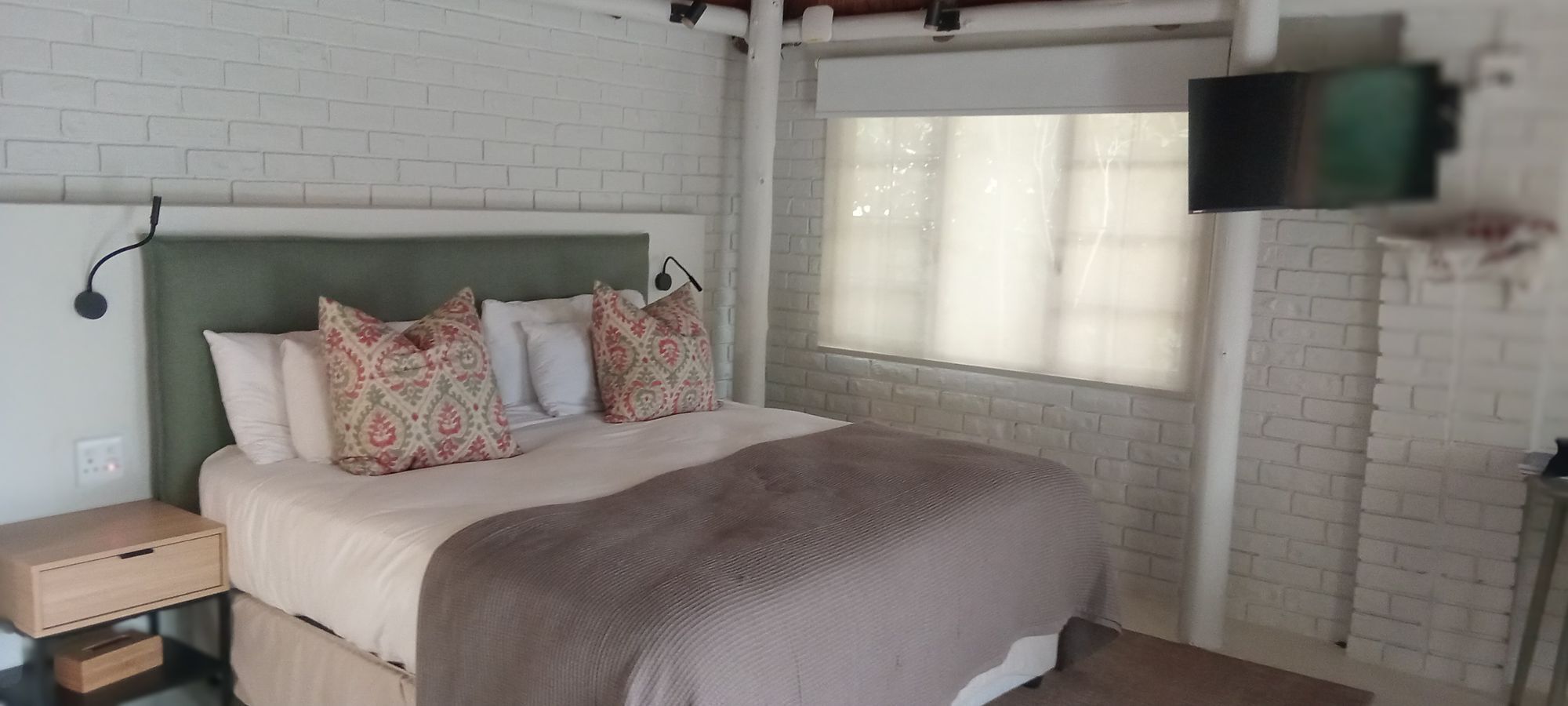 Ein Schlafzimmer mit Bett, Kissen, einem Nachttisch, einem Fernseher und einem Fenster.