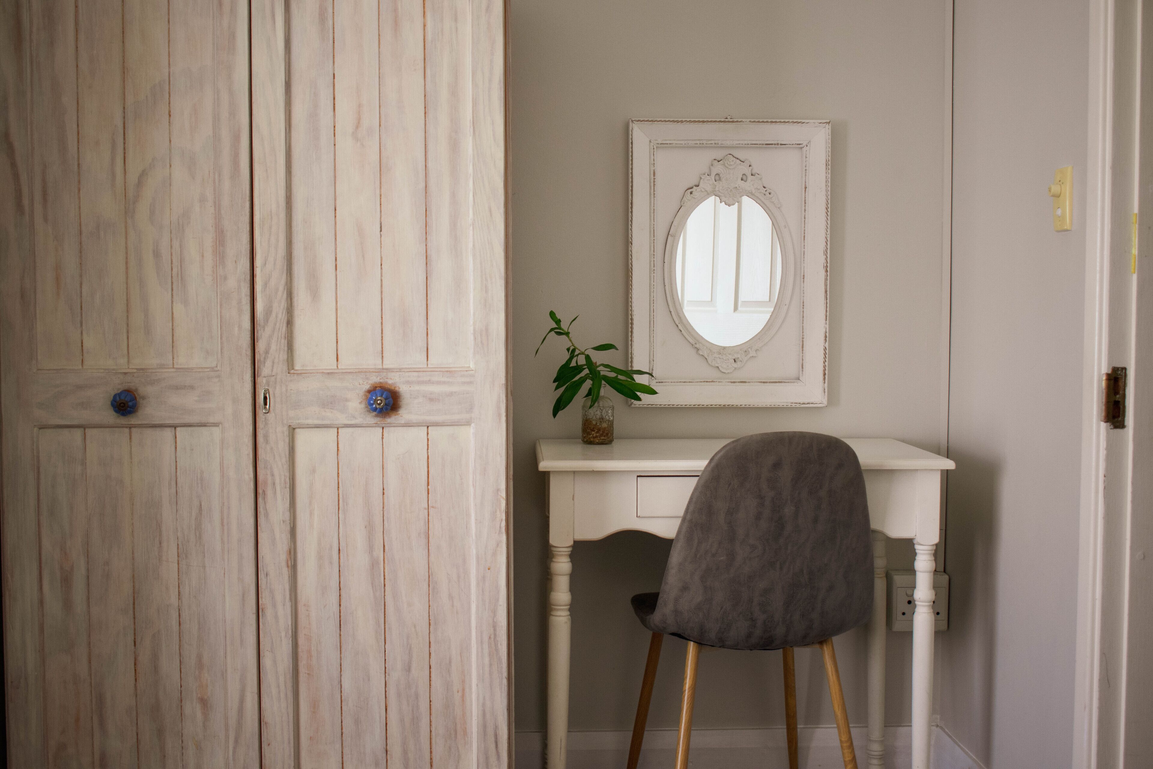 Una habitación con un armario de madera, un escritorio blanco, una silla y un espejo.