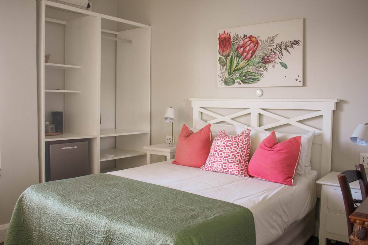 A bedroom with a bed, a wardrobe, a nightstand, and a wall-mounted lamp.
