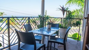 Een balkon met een tafel en stoelen, omringd door plantenbakken en uitzicht op de straat.