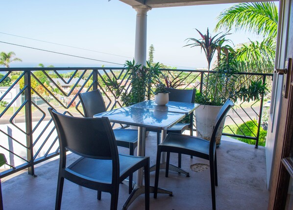 A balcony with a table and chairs, surrounded by potted plants and a view of the street.