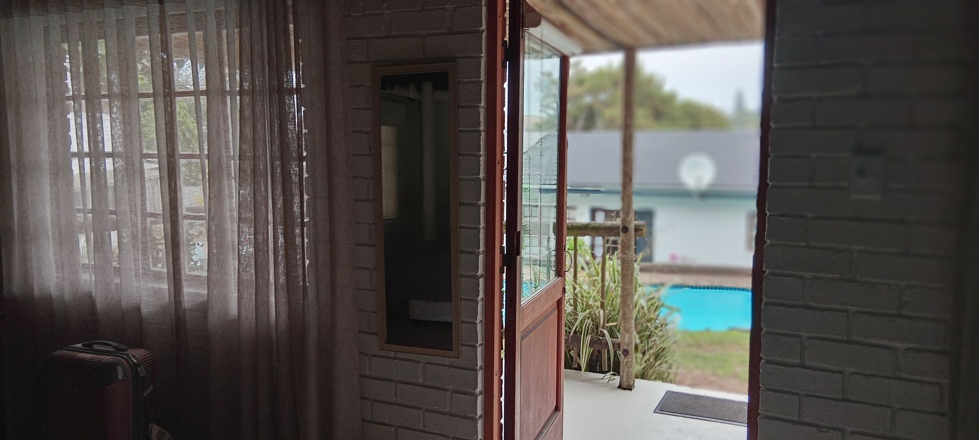 A room with a view of a swimming pool through a glass door.
