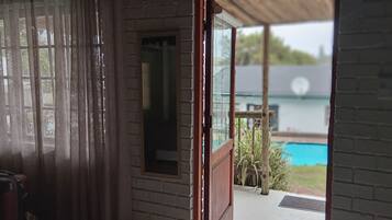 A room with a view of a swimming pool through a glass door.