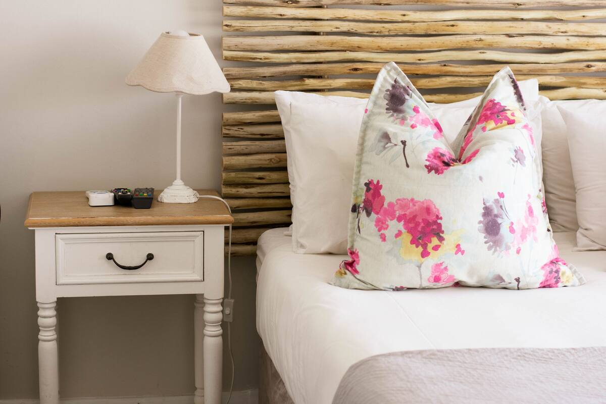 A neatly made bed with a floral pillow, a bedside table with a lamp, and a wooden headboard.
