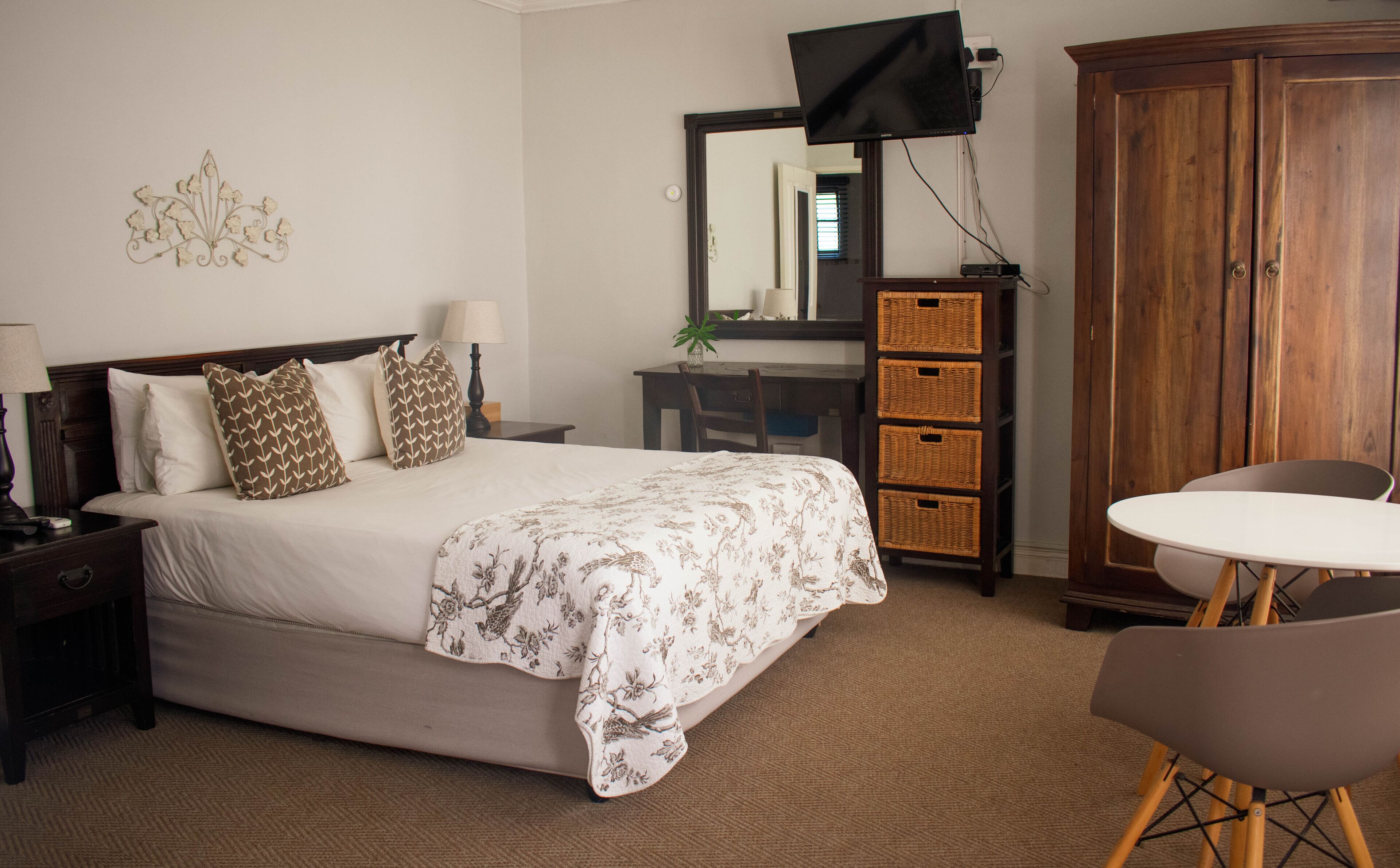 Une chambre à coucher comprenant un lit, une table de chevet, une lampe, une commode, un miroir, un téléviseur et une petite table ronde avec une chaise.
