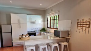 Een moderne keuken met witte kasten, een ingebouwde oven, een magnetron en een spoelbak. Drie witte barkrukken en een klein eiland met een spoelbak.