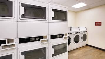 A laundry facility with multiple stacked washing machines and dryers, a wooden floor, and a sign indicating cycle times.
