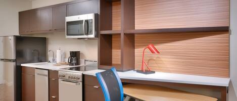 A compact kitchen with modern appliances, a built-in microwave, and a wooden desk with a chair.