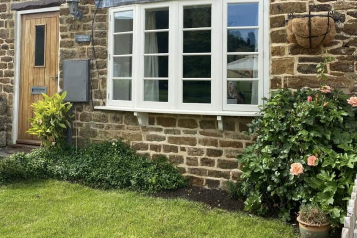 A stone house with a window, a door, and a small garden with a potted plant.
