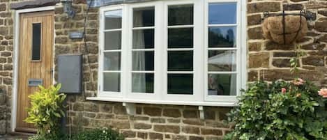 Una casa de piedra con una ventana, una puerta y un pequeño jardín con una planta en maceta.