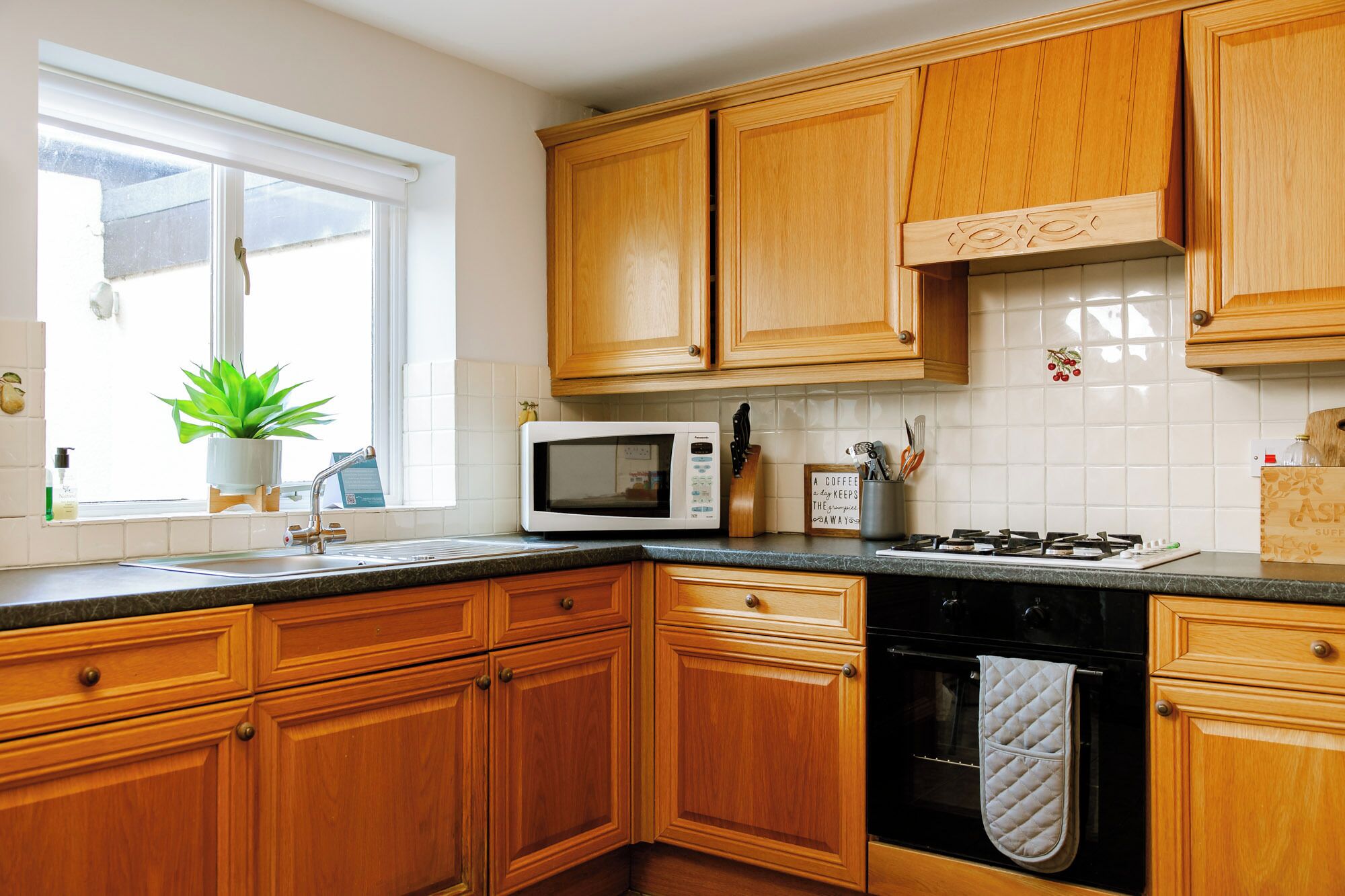 Una cocina con armarios de madera, microondas, estufa a gas y una ventana con planta.