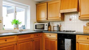 Una cocina con armarios de madera, microondas, estufa a gas y una ventana con planta.