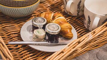 A breakfast tray with croissants, jam, honey, and coffee cups on a wicker table.