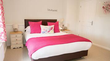 A neatly made bed with a white and pink color scheme, a headboard, and a bedside table with a lamp.