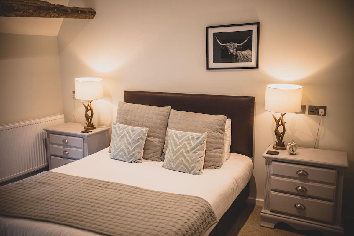 A neatly arranged bedroom with a large bed, two bedside tables with lamps, a framed picture on the wall, and a radiator under the window.