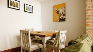 Uma sala de jantar com uma mesa de madeira e cadeiras brancas, um sofá verde e duas fotografias emolduradas na parede.
