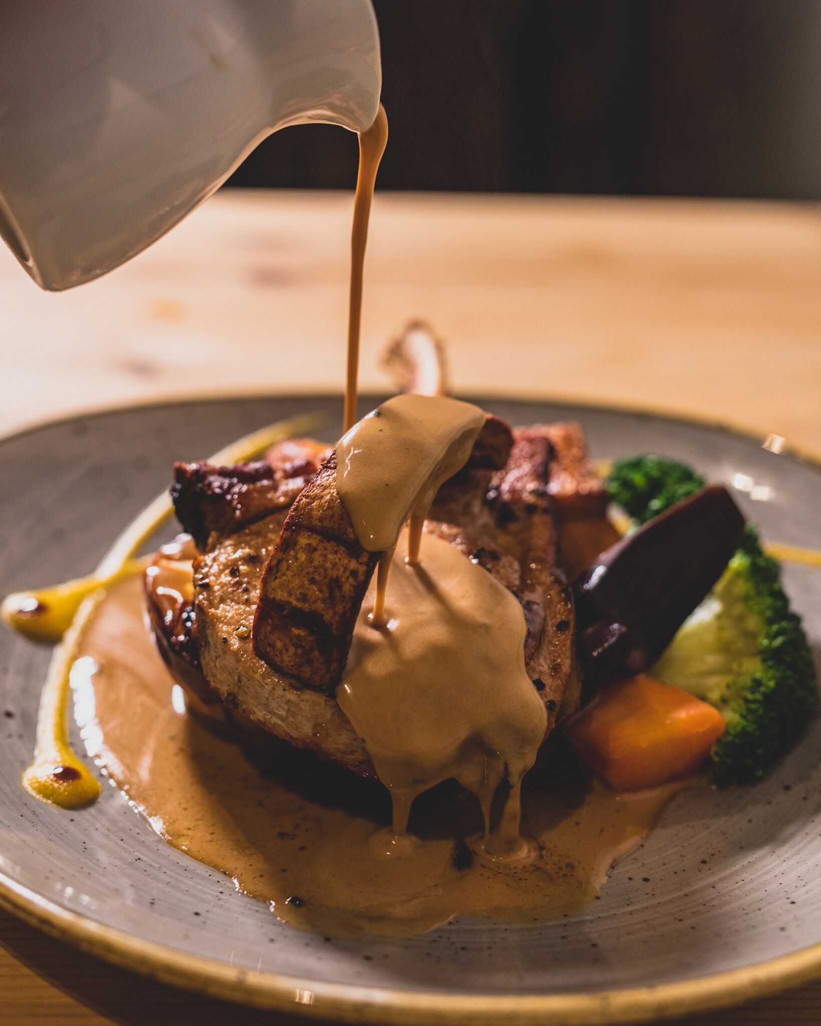 A plate of food with a steak, vegetables, and sauce.