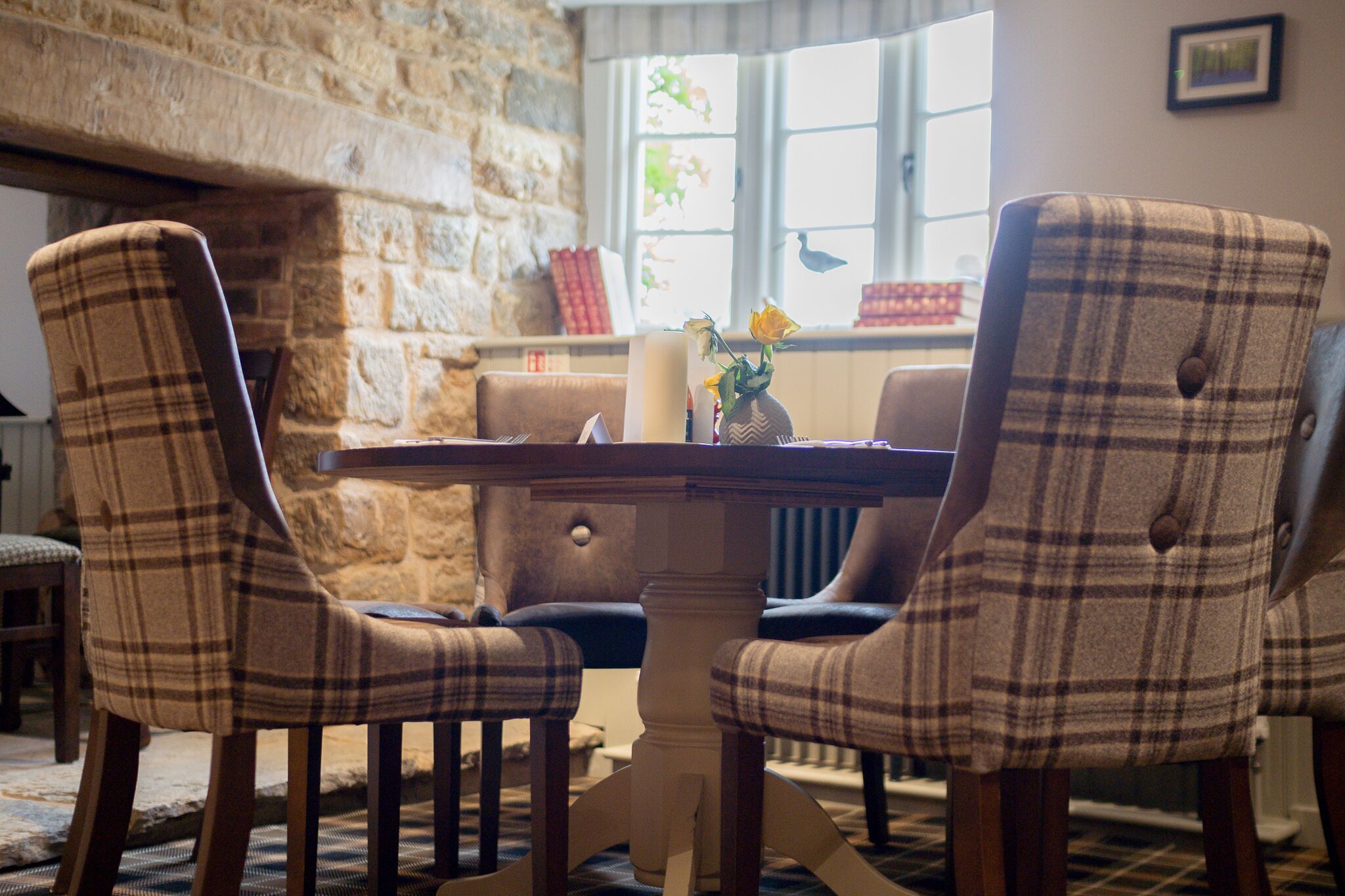 A dining area with a stone wall, a table, and four plaid chairs.