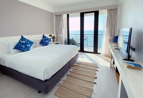 Una habitación de hotel con una cama grande, un escritorio con una computadora y vistas al mar a través de una puerta corrediza.