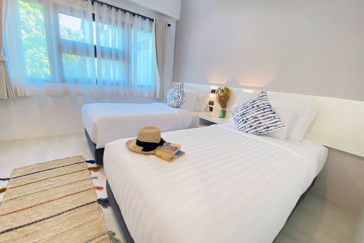 A hotel room with two beds, a striped rug, a hat, and a book on the first bed.
