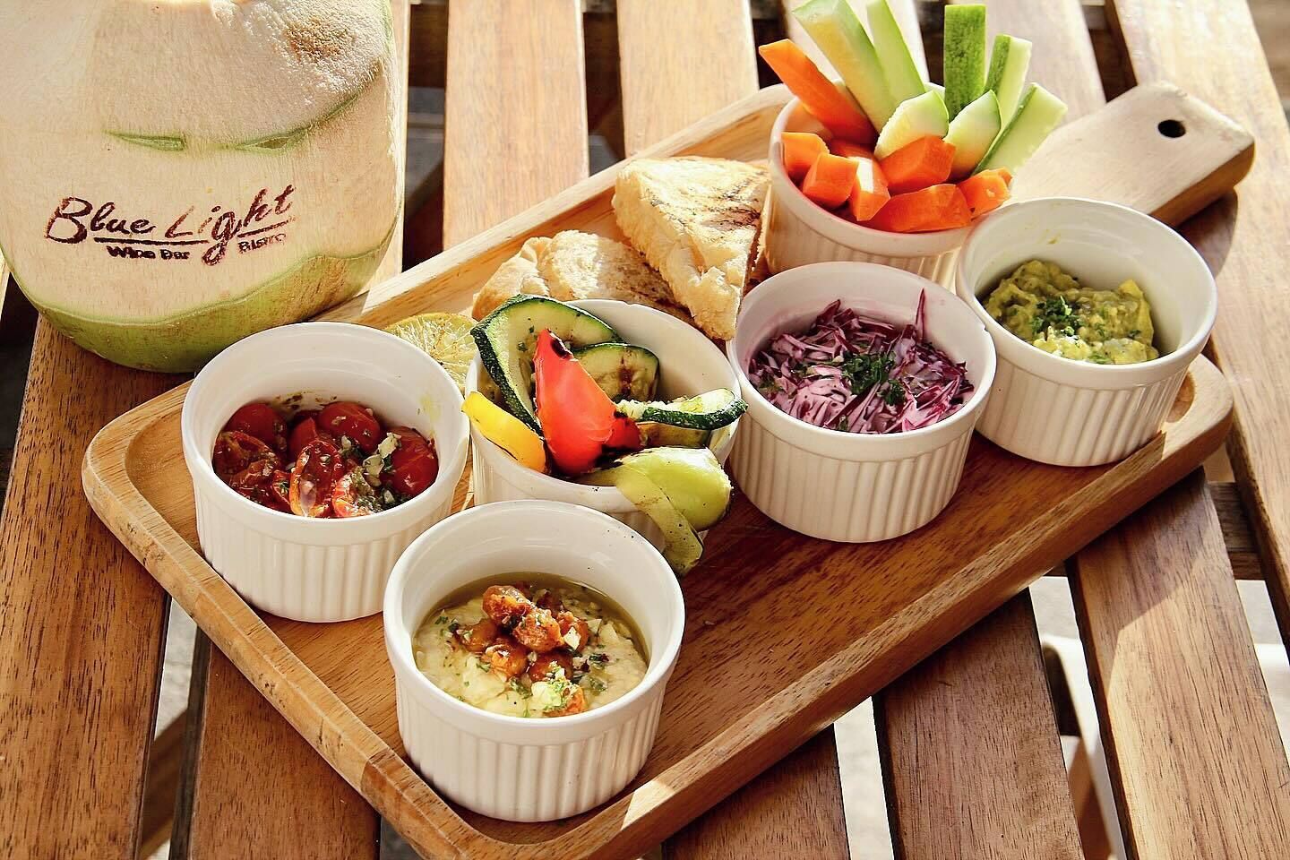 Un plateau en bois contenant divers aliments, notamment une carafe portant l’inscription « Blue Light Wine Bar », une sélection de légumes et plusieurs petits bols contenant différentes sauces.