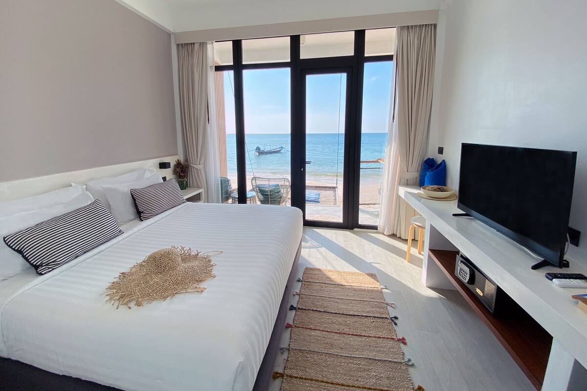 A bedroom with a large bed, a TV, and a view of the beach.