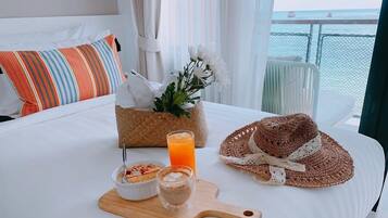 Un lit bien fait, agrémenté d’un coussin à rayures, un panier tressé rempli de fleurs, un chapeau, et des éléments de petit-déjeuner, notamment un bol de céréales, un verre de jus d’orange et une tasse de café.