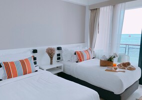 A hotel room with two beds, a small table, and a view of the sea.