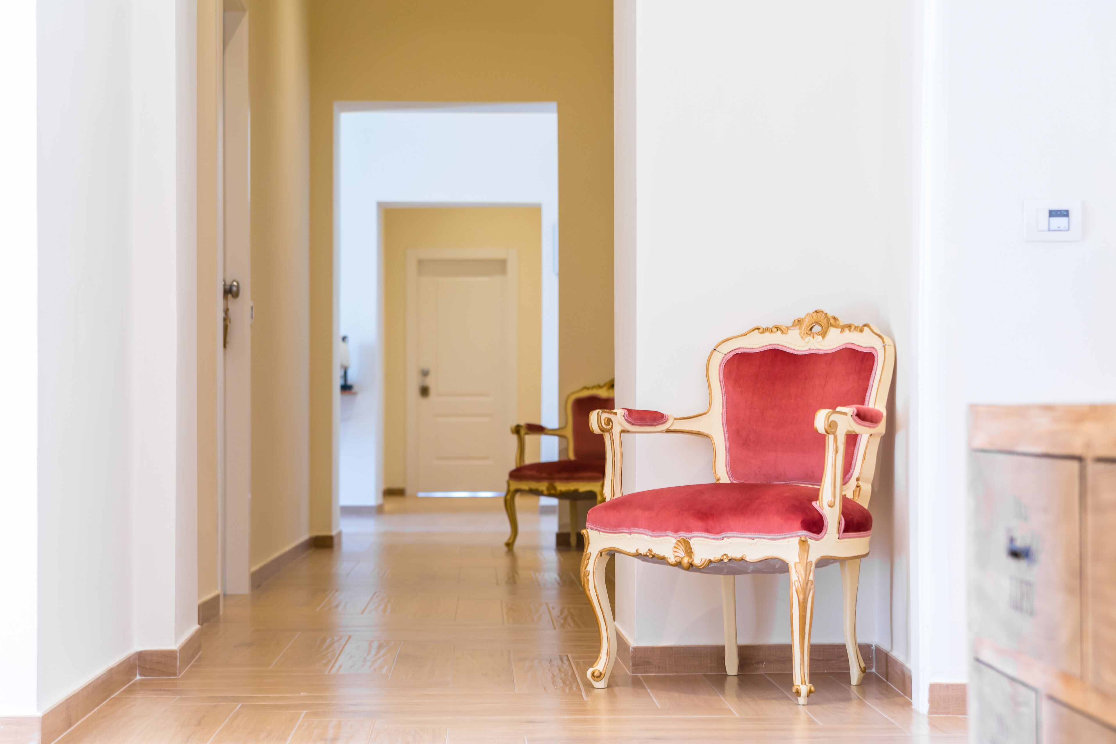 A hallway with a red upholstered chair and a wooden cabinet.