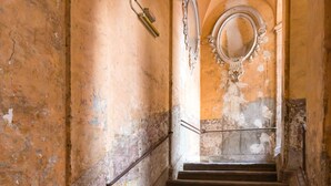 Una scala con pavimento a scacchi conduce a una stanza con uno specchio grande e decorazioni murali elaborate.