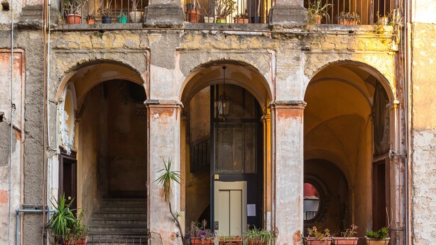 Un edificio a più piani con balconi ad arco, piante in vaso e una scala che conduce a un piano superiore.