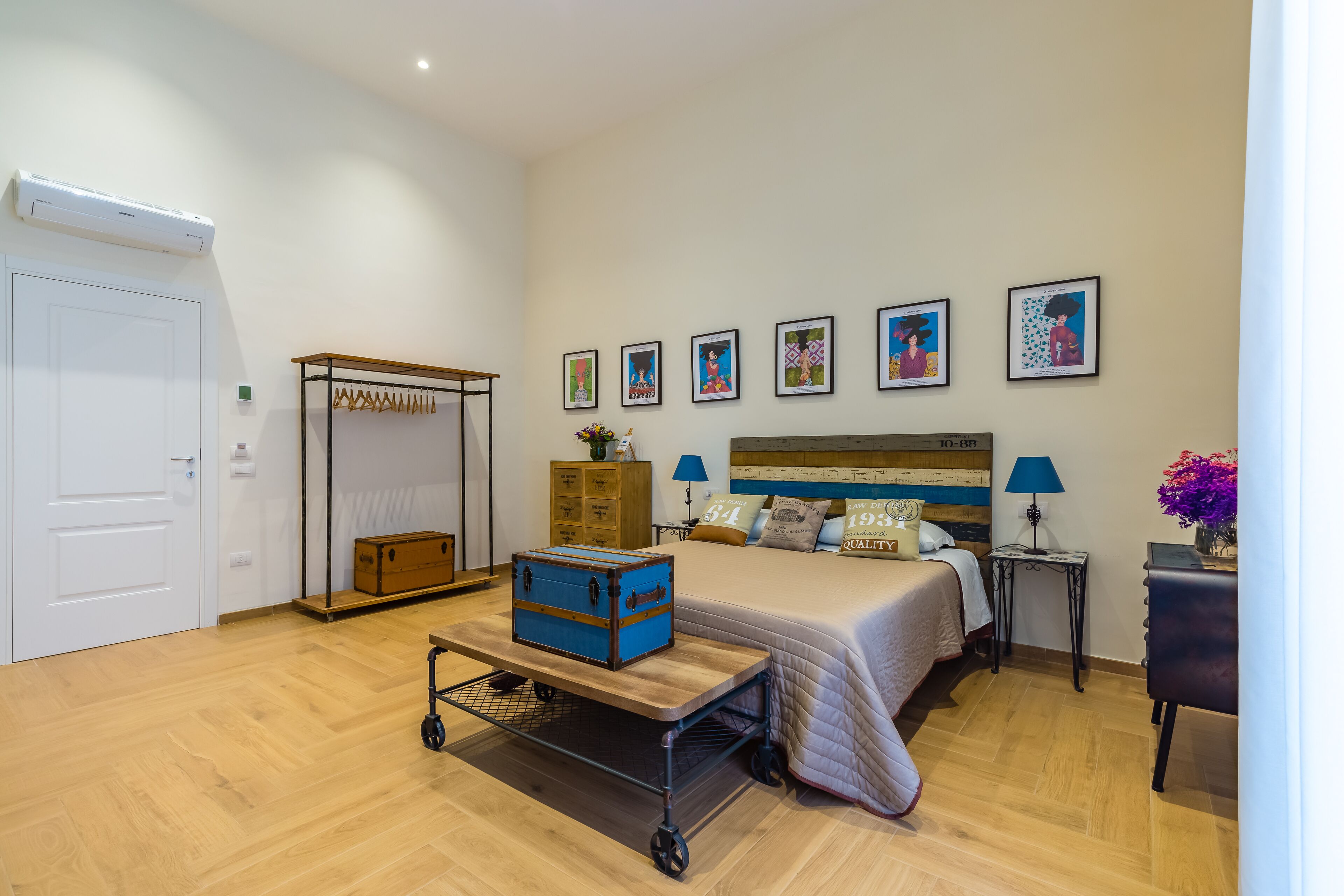 A bedroom with a bed, a dresser, a chest of drawers, a cart, and artwork on the wall.