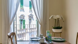 Un'area pranzo con un tavolo apparecchiato per due, una sedia, una pianta in vaso e vista su un edificio con persiane verdi.