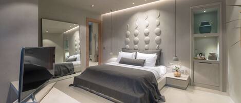 A modern bedroom with a large bed, a bedside table, a TV, and a built-in shelf with decorative items.
