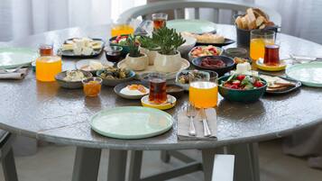 A round dining table with various dishes, drinks, and a potted plant in the background.