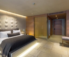 A modern bedroom with a large bed, bedside tables, a nightstand, a lamp, a sliding door, and a wooden bench. - Omm Inn (Eskisehir)