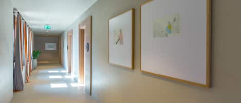 A hallway with framed artworks on the walls, a potted plant, and a sign indicating an exit.