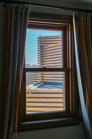 A window with wooden blinds and curtains, offering a view of a building with a sloped roof. - Omm Inn (Eskisehir)
