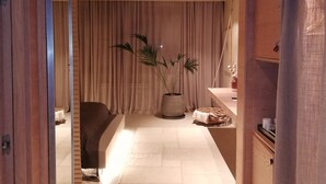 A modern hotel corridor with wooden paneling, a large potted plant, a seating area, and a counter with amenities. - Omm Inn (Eskisehir)