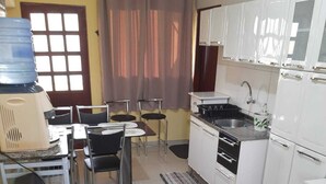 A compact kitchen with a sink, stove, and cabinets. There is a dining area with chairs and a table.