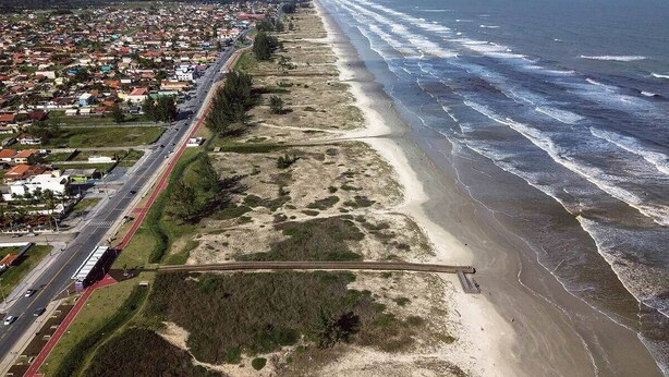 An aerial view of a coastal town with a long beach, a road parallel to the shore, and a bridge crossing the beach.