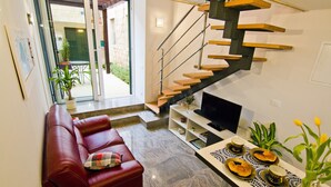 Uma sala de estar moderna com um sofá de couro vermelho, uma área de jantar com mesa posta para quatro pessoas e uma escada com degraus de madeira e corrimão de metal.